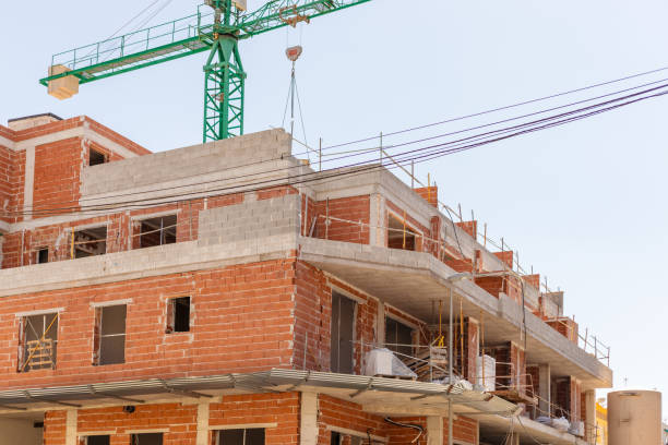 Vivid capture of construction site showcasing building in progress with brickwork and crane lifting materials. Ideal for real estate, development projects, and construction industry themes.
