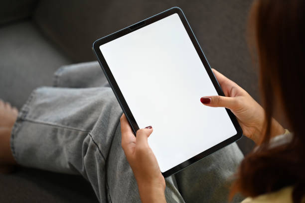 istock Young woman sitting in cozy sofa holding digital tablet with white blank screen 2165980406
