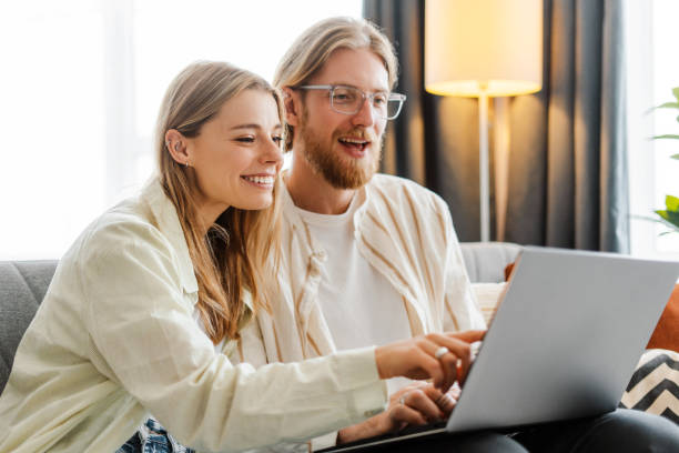 istock Young couple sitting on sofa at home and using laptop computer 2165986707