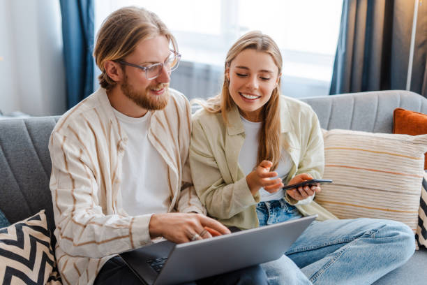 Young couple sitting on sofa using laptop and smartphone for online shopping