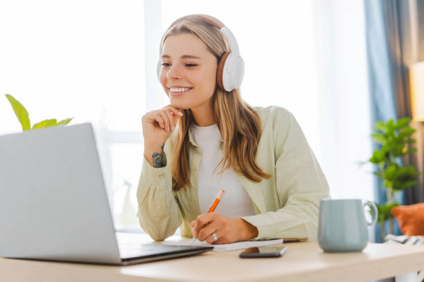 istock Young woman wearing headphones taking notes while attending online class 2165986739