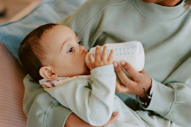 Medium close up of caring female hands holding her son and bottle with formula to feed baby