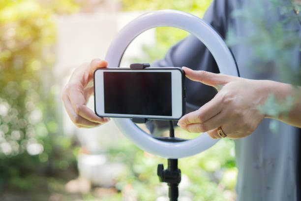 istock Unrecognizable woman preparing smartphone in tripod with ring lamp before shooting vlog at outdoor. 2165991733