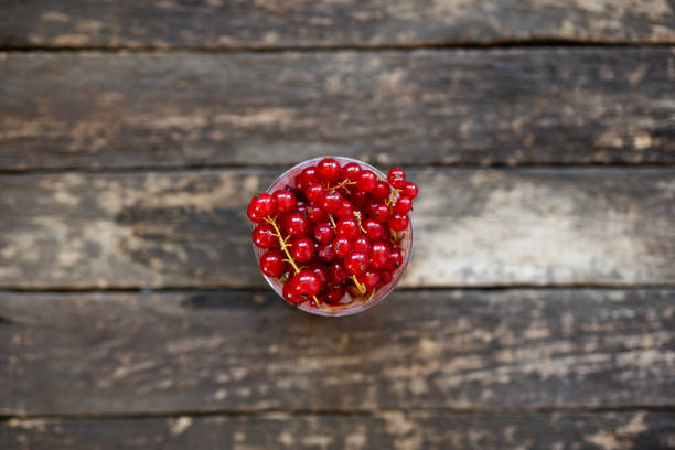 Fresh red currant berries in a glass on a wooden background.