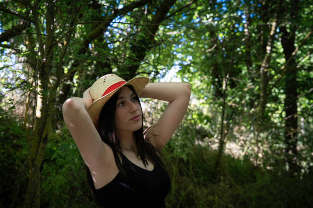 In a natural environment with green vegetation, a beautiful girl with long brown hair and a hat, is observing the nature with interest.
