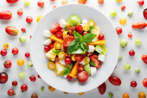 Salad with different varieties kind of red, yellow, green and black tomato mix, mozzarella cheese and basil. Caprese salas with fresh colourful tomatoes. Food photography
