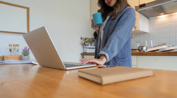 istock Woman Working from Home in Dining Room with Laptop and Coffee Cup in Modern Kitchen Setting 2166005606