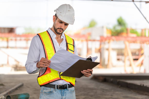 istock Engineer man with blueprint at construction site, Foreman worker in hardhat working on a construction site 2166007306