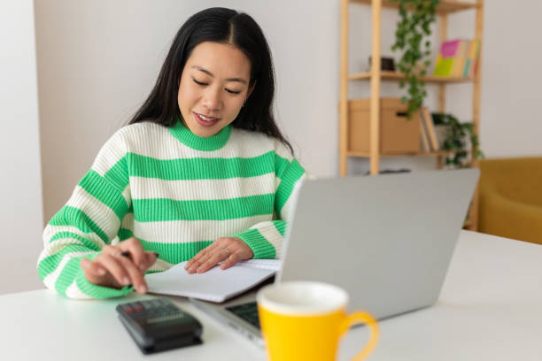 istock Young smiling freelancer asian woman working on laptop computer at home 2166020003