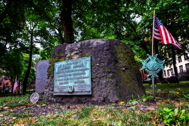 Boston, Massachusetts, USA - August 7, 2024: The grave site of Samuel Adams in Boston's Ganary Burying Ground. Samuel Adams (17221803) was an American Patriot who helped organize the American Revolution, signed the Declaration of Independence, and became Governor of Massachusetts. Selective focus.. The Granary Burying Ground in Massachusetts is the city of Boston's third-oldest cemetery, founded in 1660 and located on Tremont Street. It is the burial location of Revolutionary War-era patriots, including Paul Revere, the five victims of the Boston Massacre, and three signers of the Declaration of Independence: Samuel Adams, John Hancock, and Robert Treat Paine. The cemetery has 2,345 grave-markers, but historians estimate that as many as 5,000 people are buried in it. It is a site on Boston's Freedom Trail.