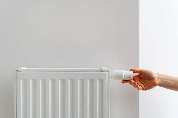 Person adjusting thermostat on radiator making comfortable temperature in room