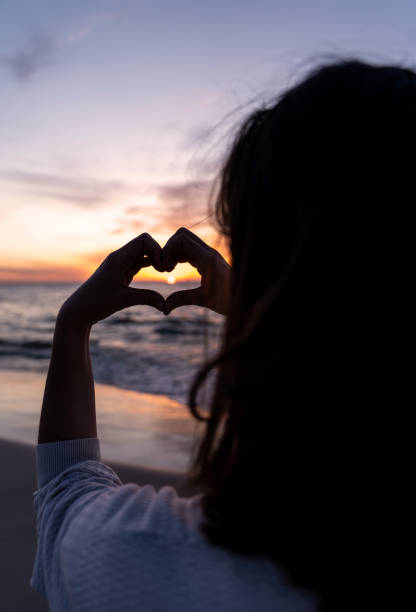 istock Romantic woman enjoying summer vacation. Making a heart shape with hands around the setting sun 2166031841