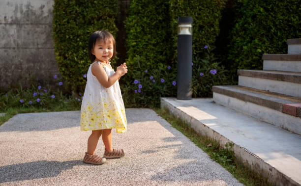 Full length of adorable little girl walking on park pathway on a sunny summer day and looking at camera
