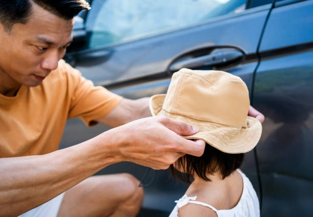 Father wearing hat on daughter's head by car outside