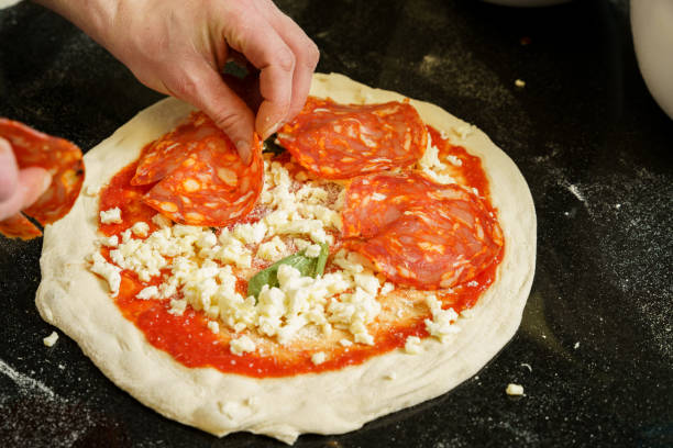 istock A chef preparing a pizza with tomato sauce and mozzarella cheese, spreading salami on pizza 2166039540