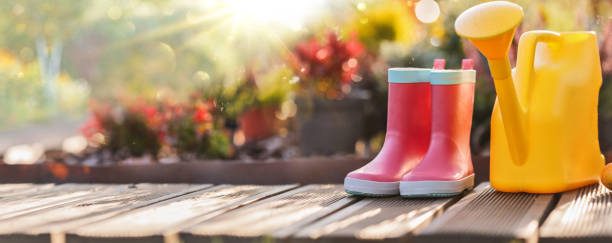 Autumn work in the garden. Wooden background with boots and yellow watering can against a backdrop of plants and sunlight