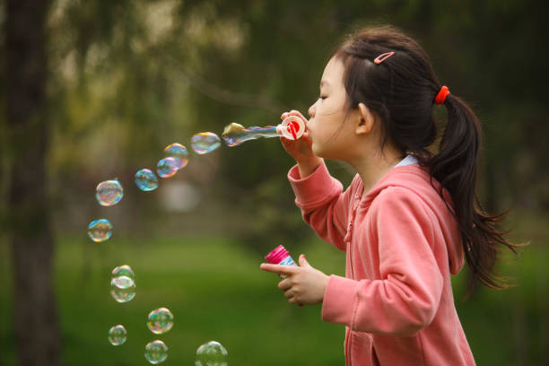 istock Kid Asian Girl Blowing Soap Bubbles in Park 2166044812