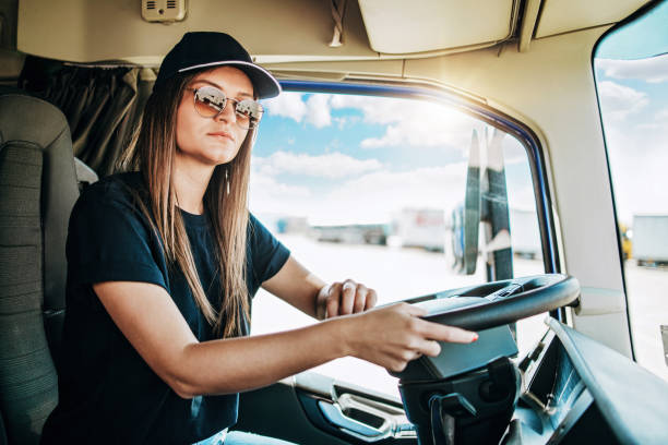 Portrait of beautiful young woman professional truck driver sitting and driving big truck. Inside of vehicle. People and transportation concept.