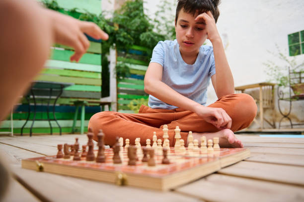 istock Boy concentrating on a chess game with his friend outdoors on a sunny day 2166053502