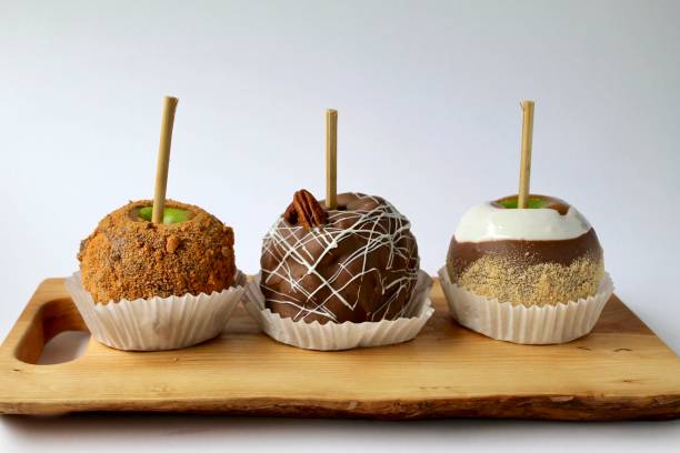 istock Three caramel apples with milk chocolate candy and nuts on a wooden cutting board 2166067073