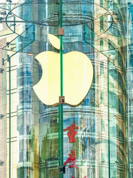 Chongqing, China - August 6, 2024. A close-up view of the Apple logo on the glass cylindrical entrance of the Apple Store in Jiefangbei CBD, Chongqing, China. Through the glass, the red Chinese characters for Chongqing can be seen on the exterior wall of a nearby building, creating a layered composition that connects the stores modern design with the citys cultural identity.