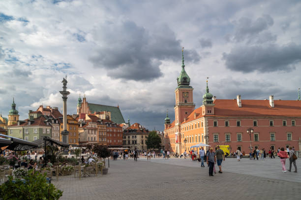 25.07.2024 Warsaw, Poland. Warsaw's Old Town Square, featuring the iconic Sigismund's Column and Royal Castle, bustles with visitors. The vibrant, colorful buildings and dramatic clouds set a picturesque scene, showcasing the rich history and lively atmosphere of Poland's capital.