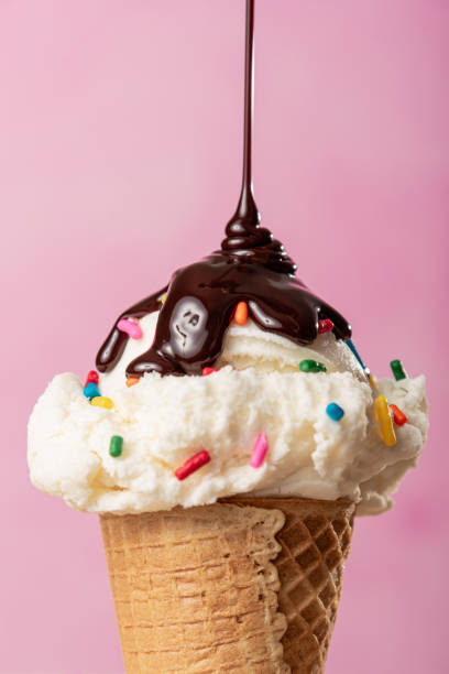 Vanilla ice cream cone with color sprinkles on top and chocolate drizzle with a pink background