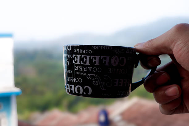 A hand holding a cup while looking at the green scenery