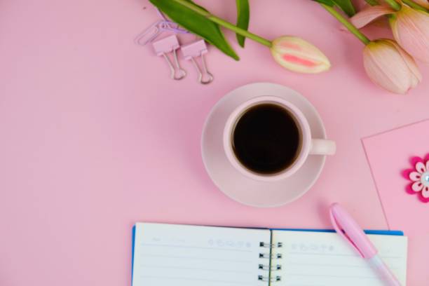 istock Flatlay of coffee with office tools, pink headphone, laptop, spectacles, notebook, pen and a bouquet of pink tulips on pink background as copy space concept 2166121225