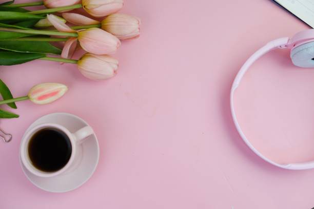 istock Flatlay of coffee with office tools, pink headphone, laptop, spectacles, notebook, pen and a bouquet of pink tulips on pink background as copy space concept 2166121233