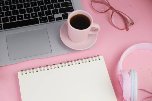 istock Flatlay of coffee with office tools, pink headphone, laptop, spectacles, notebook, pen and a bouquet of white daisy on pink background as copy space concept 2166121243