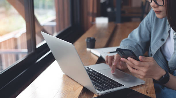 istock Business woman using mobile phone and working on laptop computer at coffee shop. Student searching the information, studying online, work from cafe, distant job, business casual 2166122187