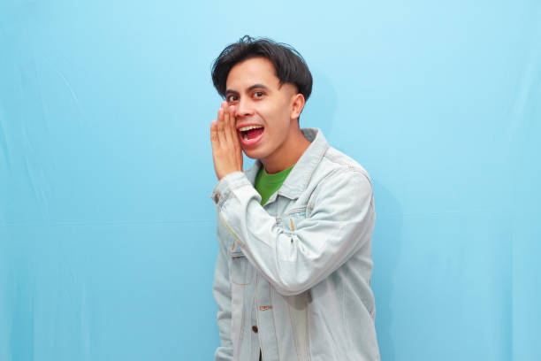 istock Young Asian man doing whisper gesture with excited face isolated on a blue background 2166124718