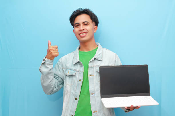 istock Young Asian man posing holding laptop computer with happy excited face on isolated blue background 2166124992