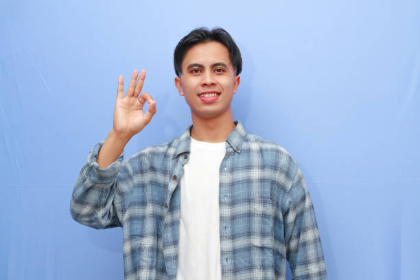 istock Handsome young Asian man posing OK sign or approve sign with hand while smiling friendly on isolated blue background 2166126081