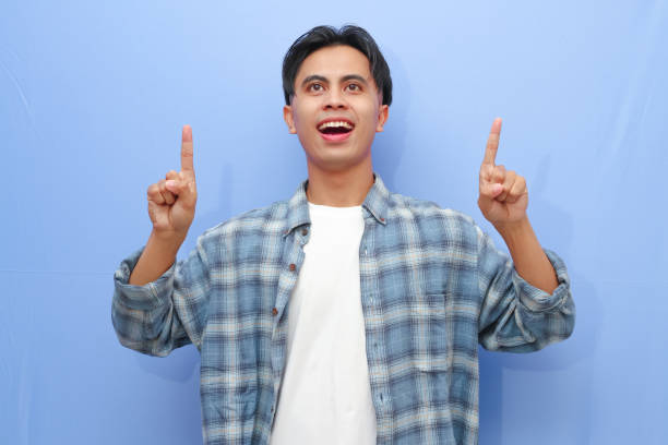 istock Excited happy young Asian man posing pointing finger to empty copy space isolated on blue background. 2166126094