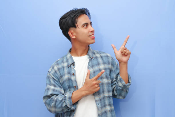 istock Excited happy young Asian man posing pointing finger to empty copy space isolated on blue background. 2166126114