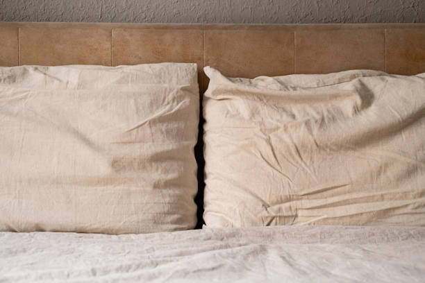 istock Two beige pillows on an unmade bed with wrinkled sheet and headboard. 2166128661