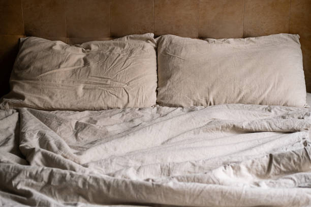 istock Wrinkled bed with beige pillows and sheets in cozy bedroom. 2166128668