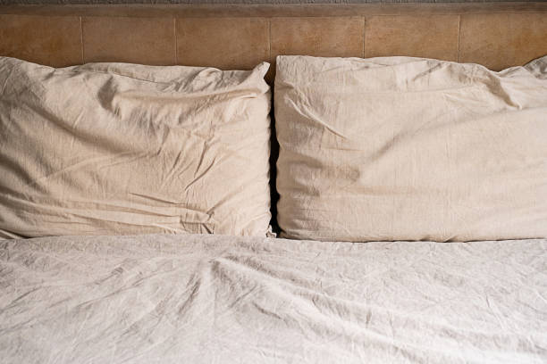 istock Two beige pillows on an unmade bed with wrinkled sheet and headboard. 2166128673