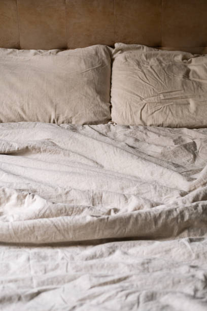 istock Wrinkled bed with beige pillows and sheets in cozy bedroom. 2166128676