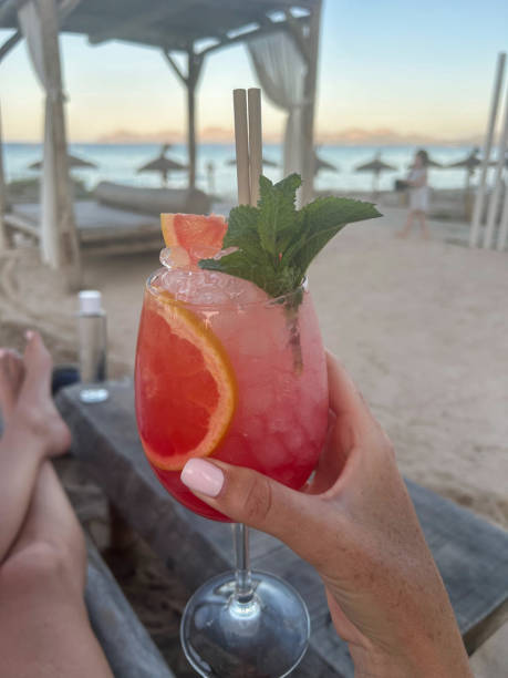 istock A white hand holds a colourful cocktail on a beach. 2166133200