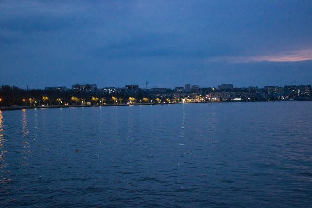 A tranquil view of a cityscape at dusk with buildings softly lit and their reflections shimmering in the calm water of the waterfront.