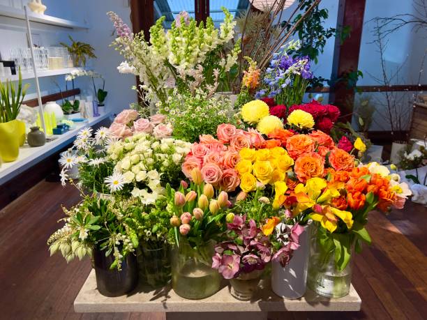 Horizontal closeup photo of bunches of colourful fresh flowers in containers on display for sale in a Florist Shop.