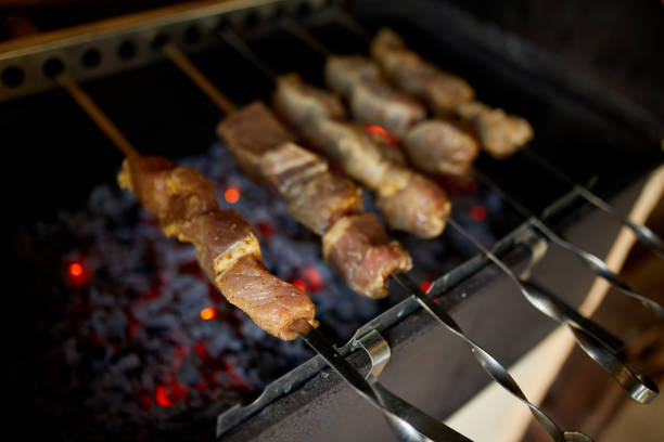 Skewers of kebabs cook over the hot coals of a barbecue grill in a home backyard setting, highlighting a summer culinary tradition.