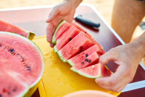 istock Man Slicing Fresh Watermelon on a Yellow Cutting Board Outdoors in Summertime 2166143655