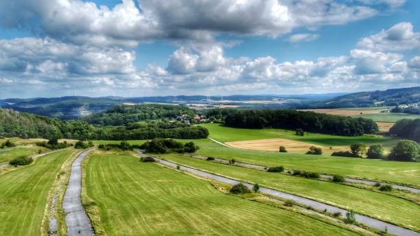 istock A road runs through a lush green field with a cloudy sky in the background 2166148178