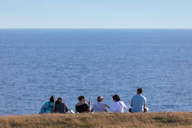 A family sitting at a hilltop on the Scania coast at Ales Stenar with a view of the Baltic Sea.