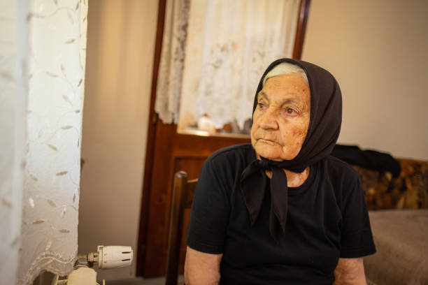 Old lonely woman sitting near the window in her house