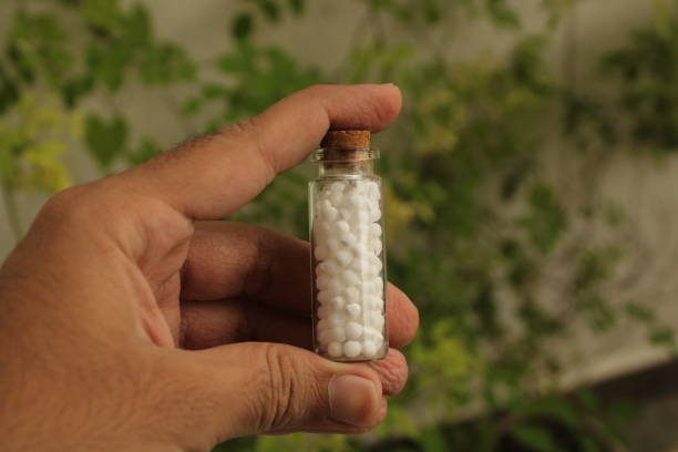 Homoeopathy medicine and nature. A view of human hand holding a glass bottle with homoeopathic medicine. Natural background. Homoeopathy and nature. rajkot india stock pictures, royalty-free photos & images